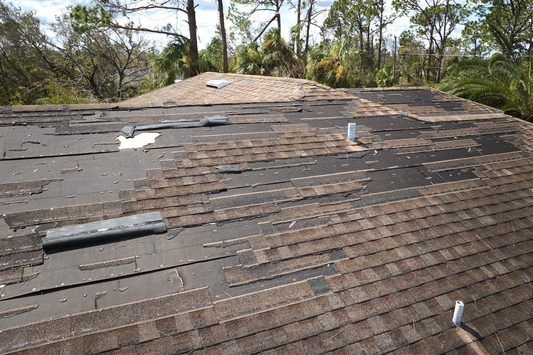 Damaged house roof with missing shingles after hurricane Ian in Florida. Consequences of natural disaster like storm